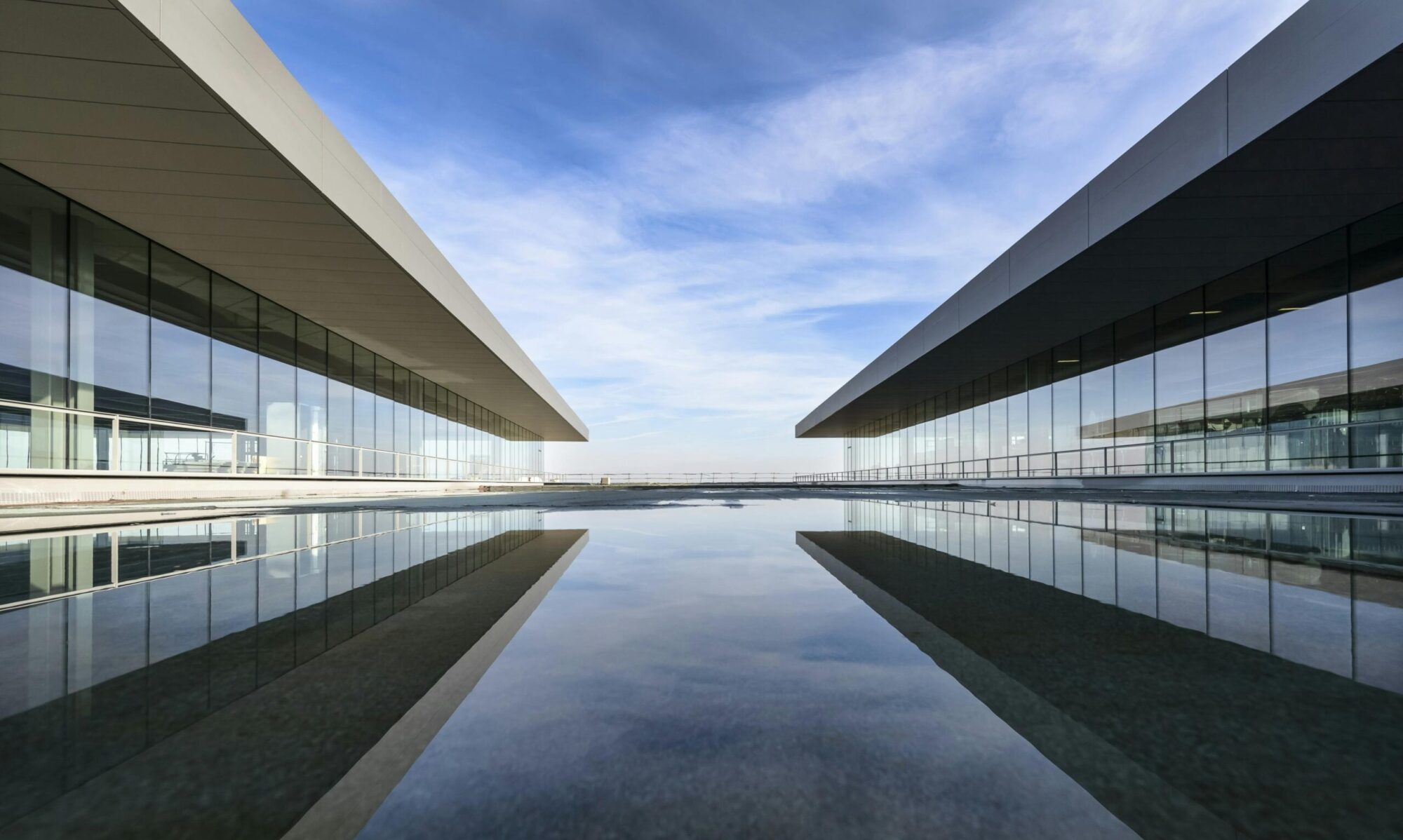 Futuristic glass building mirrored on a still water surface with a cloudy sky.